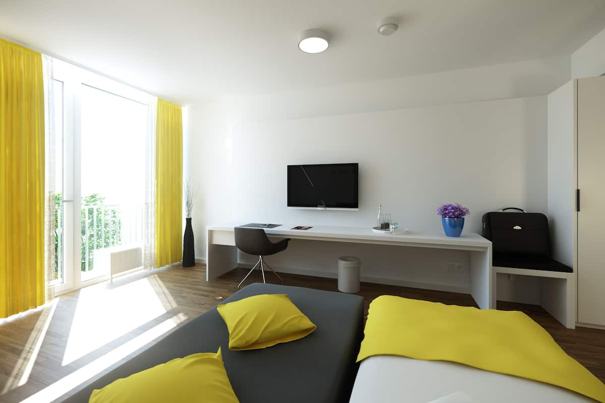 A modern hotel room with a bed, a desk, a chair, a television, and a suitcase.