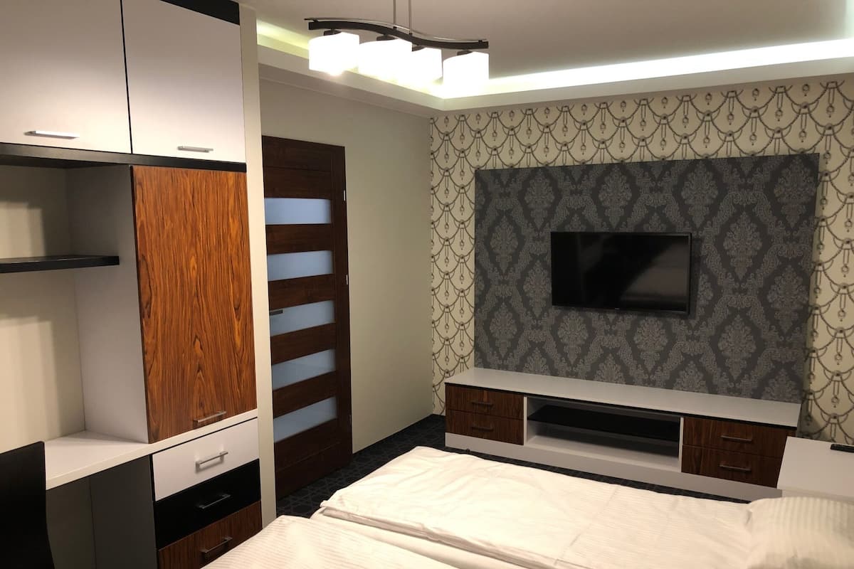 A modern bedroom with a bed, a TV mounted on the wall, and a wardrobe with a mirror.