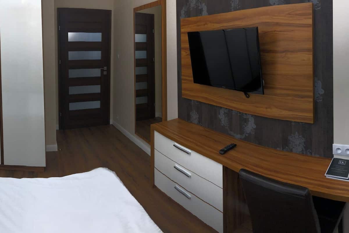 A hotel room with a bed, bedside tables, a TV mounted on the wall, and a wardrobe.