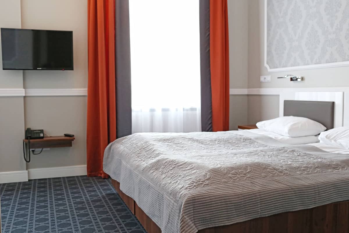 A hotel room with a bed, a television mounted on the wall, a telephone, and a window with curtains.