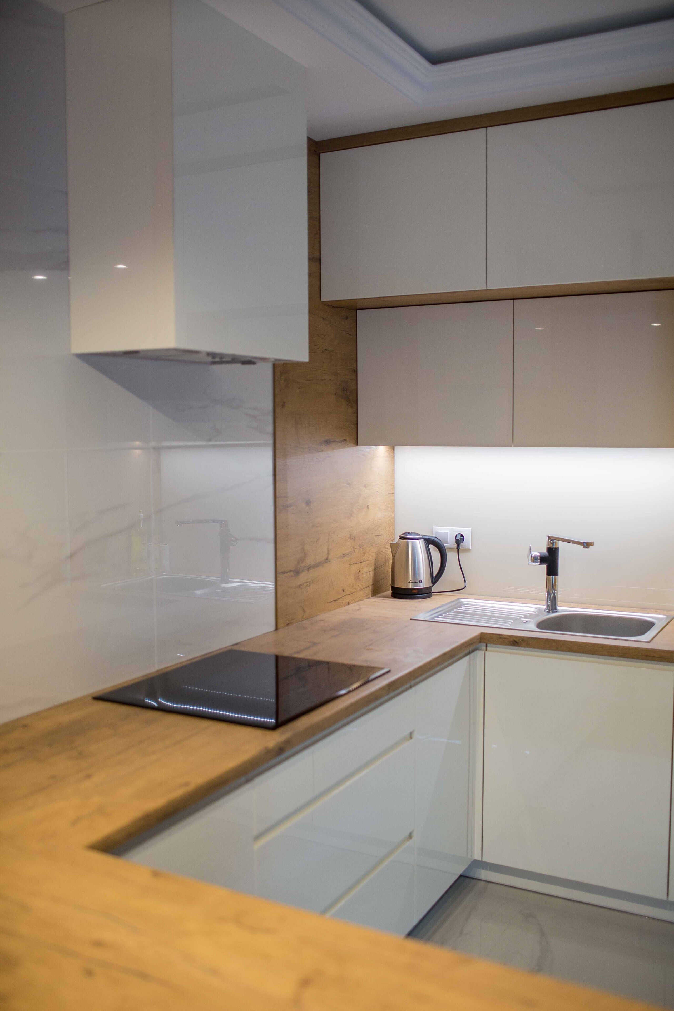 A modern kitchen with white cabinets, a wooden countertop, a kettle, and a sink.
