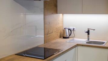 A modern kitchen with white cabinets, a wooden countertop, a kettle, and a sink.