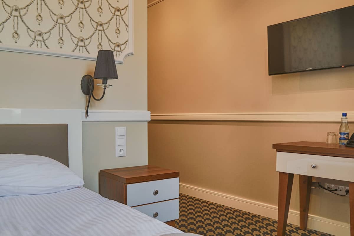 A hotel room with a bed, a bedside table with drawers, a lamp, a wall-mounted phone, and a television.