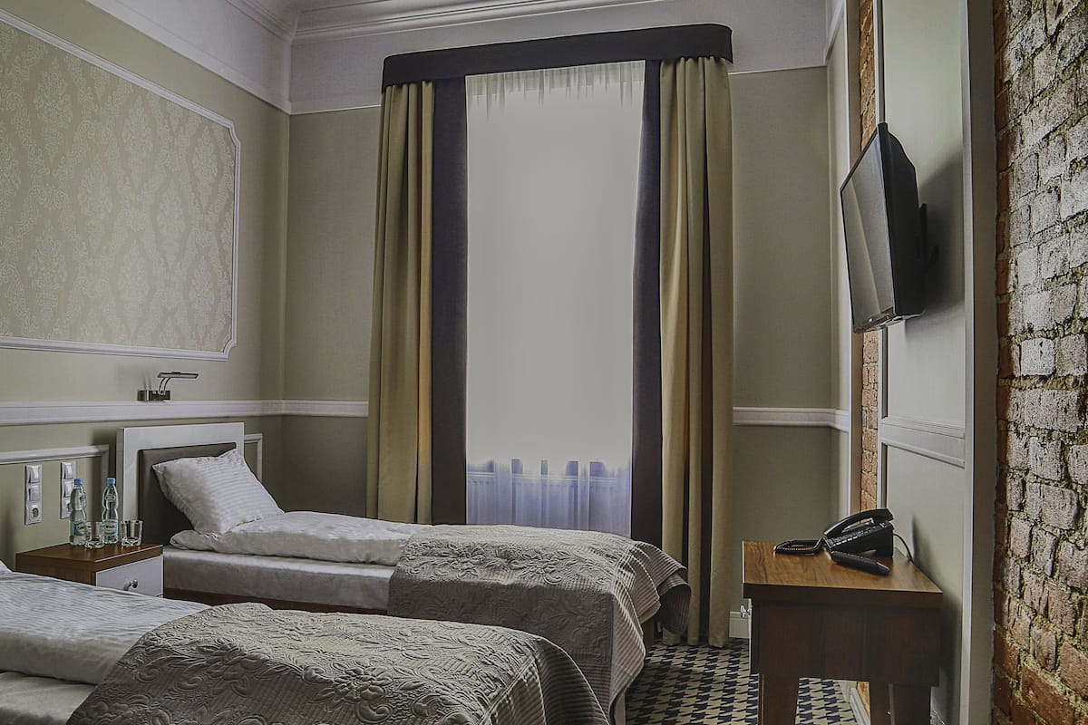 A hotel room with two beds, a TV mounted on the wall, a bedside table with a phone, and a window with curtains.