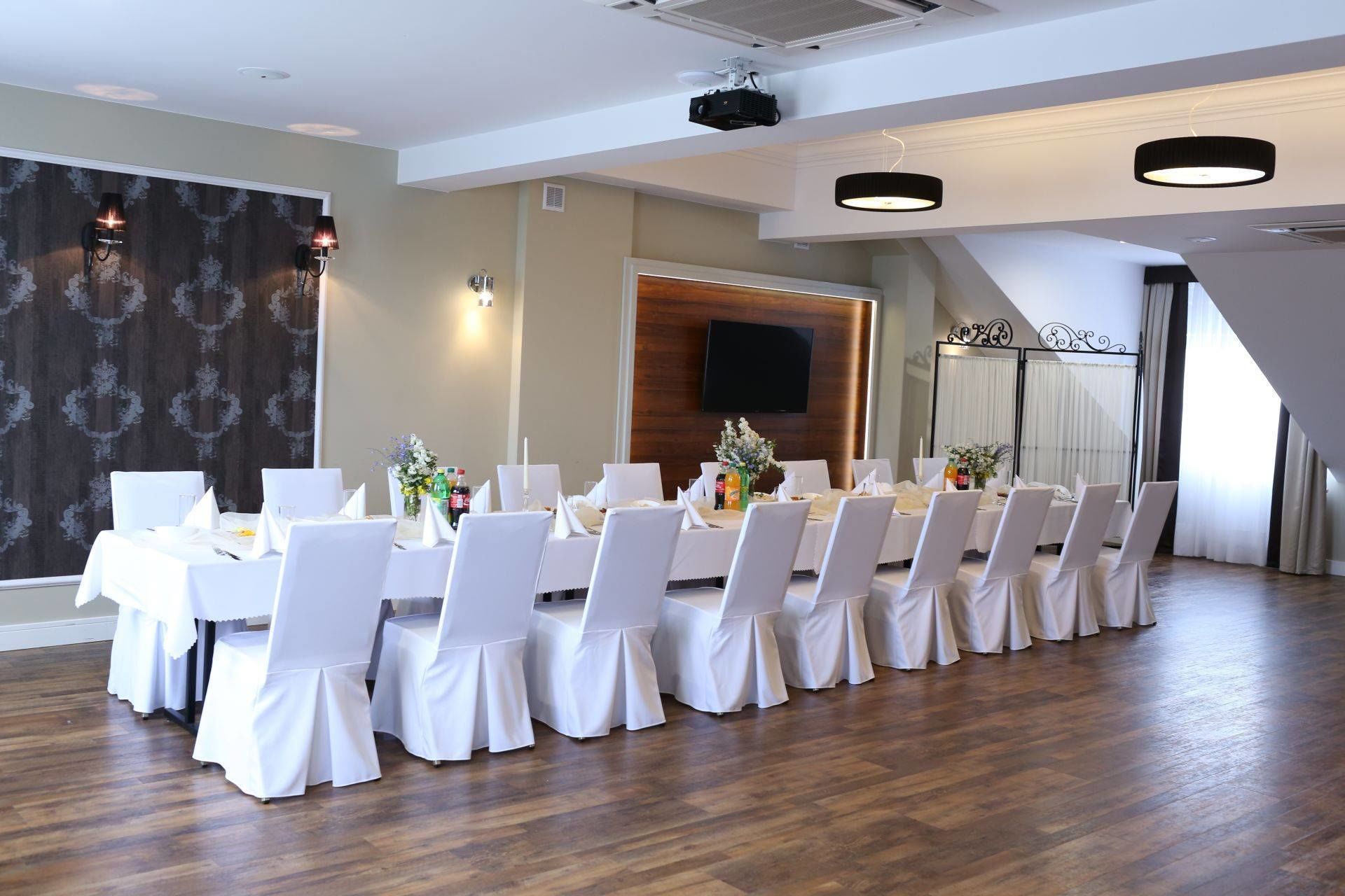 A conference room with a long table, white chairs, and a wooden panel wall with a TV.