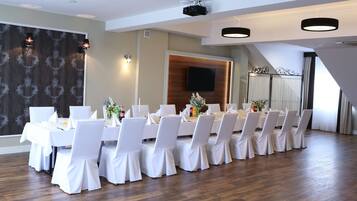 A conference room with a long table, white chairs, and a wooden panel wall with a TV.