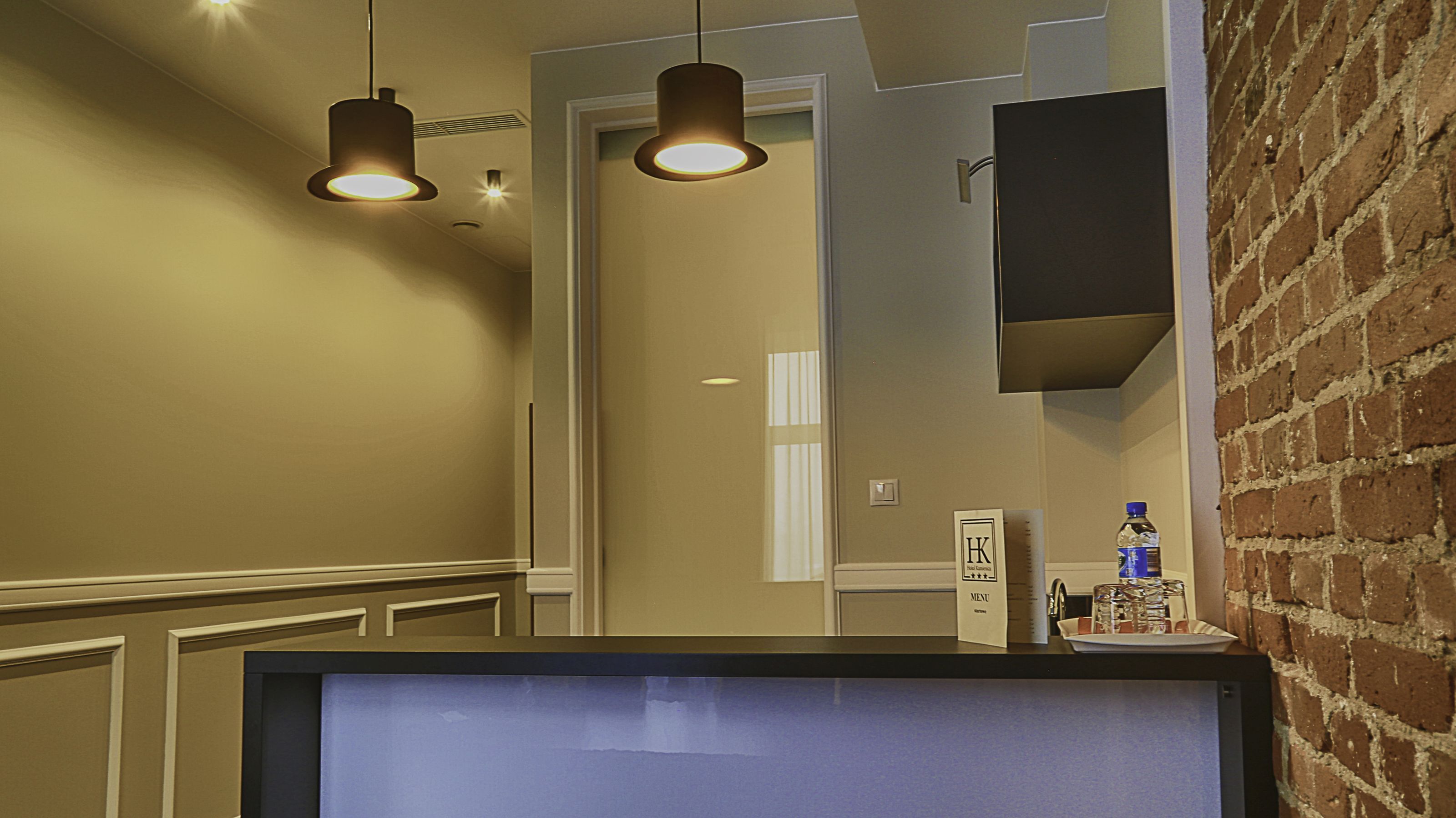 A hallway with a television on a counter, a brick wall, and pendant lighting.