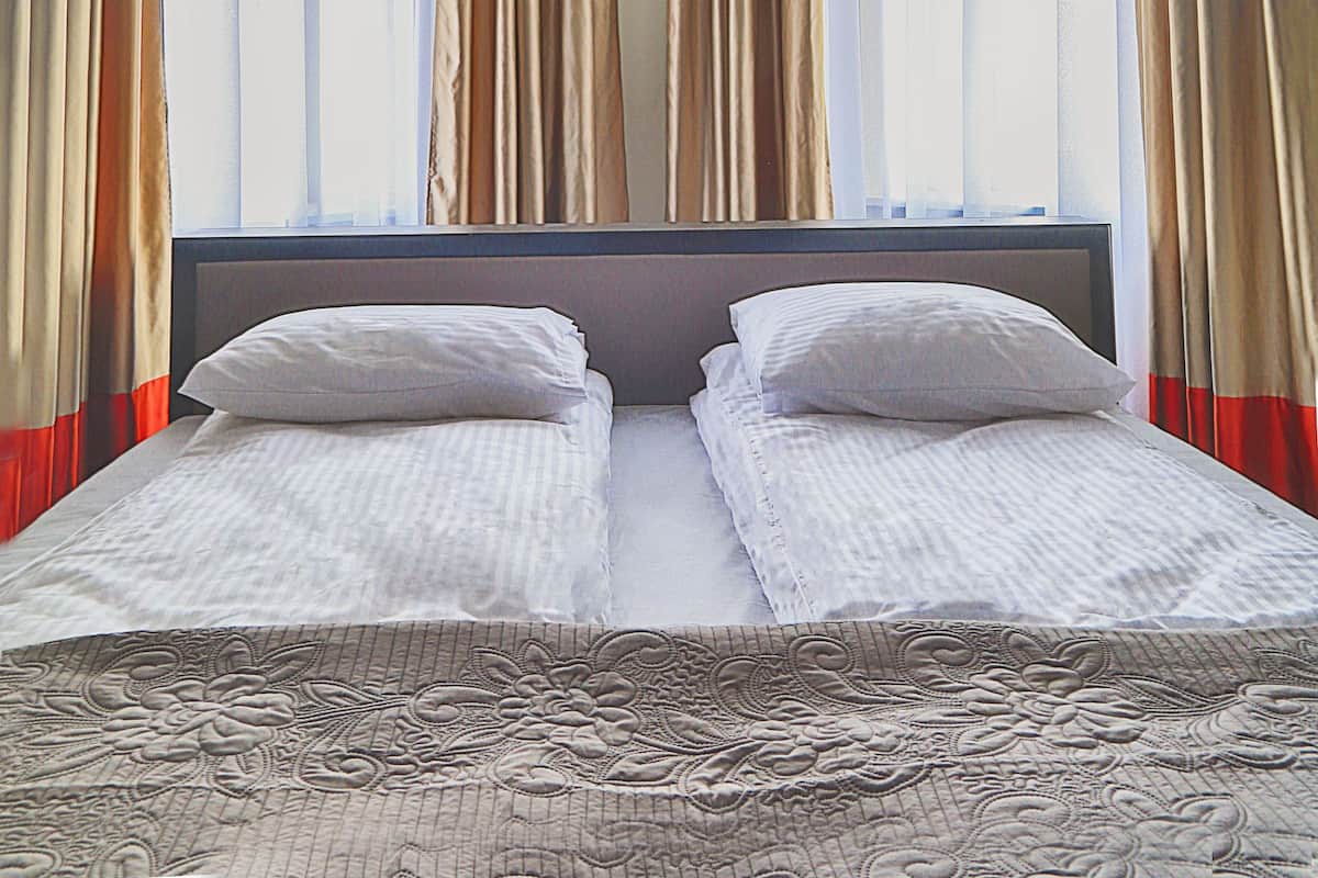 A hotel room with two beds, a large window with curtains, and two wall-mounted lamps.