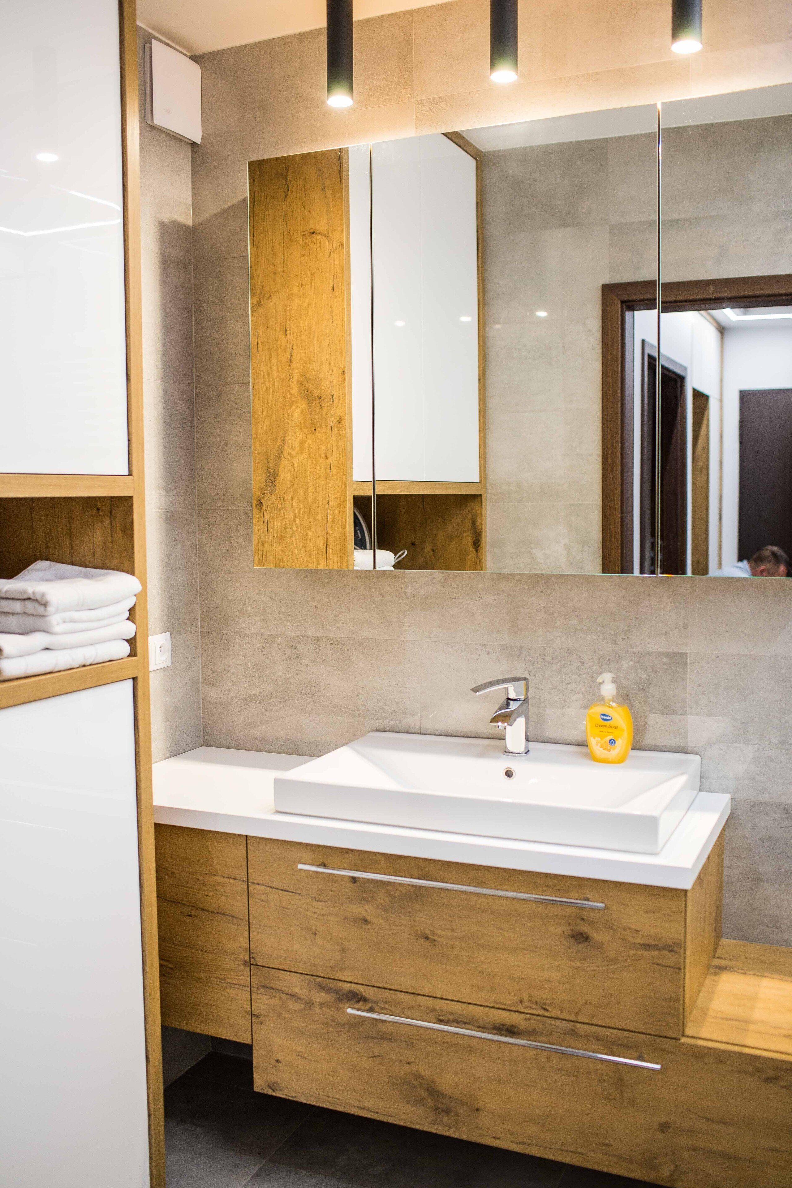 Un baño moderno con un lavabo blanco, tocador de madera y un espejo grande.
