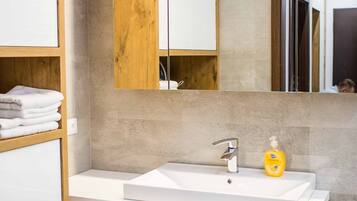 Un baño moderno con un lavabo blanco, tocador de madera y un espejo grande.