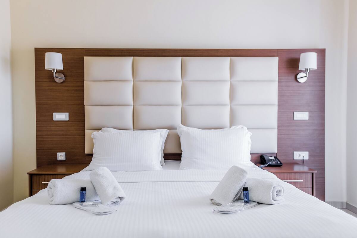 Une chambre d’hôtel avec un grand lit, deux tables de chevet, une tête de lit en bois et deux lampes fixées au mur.
