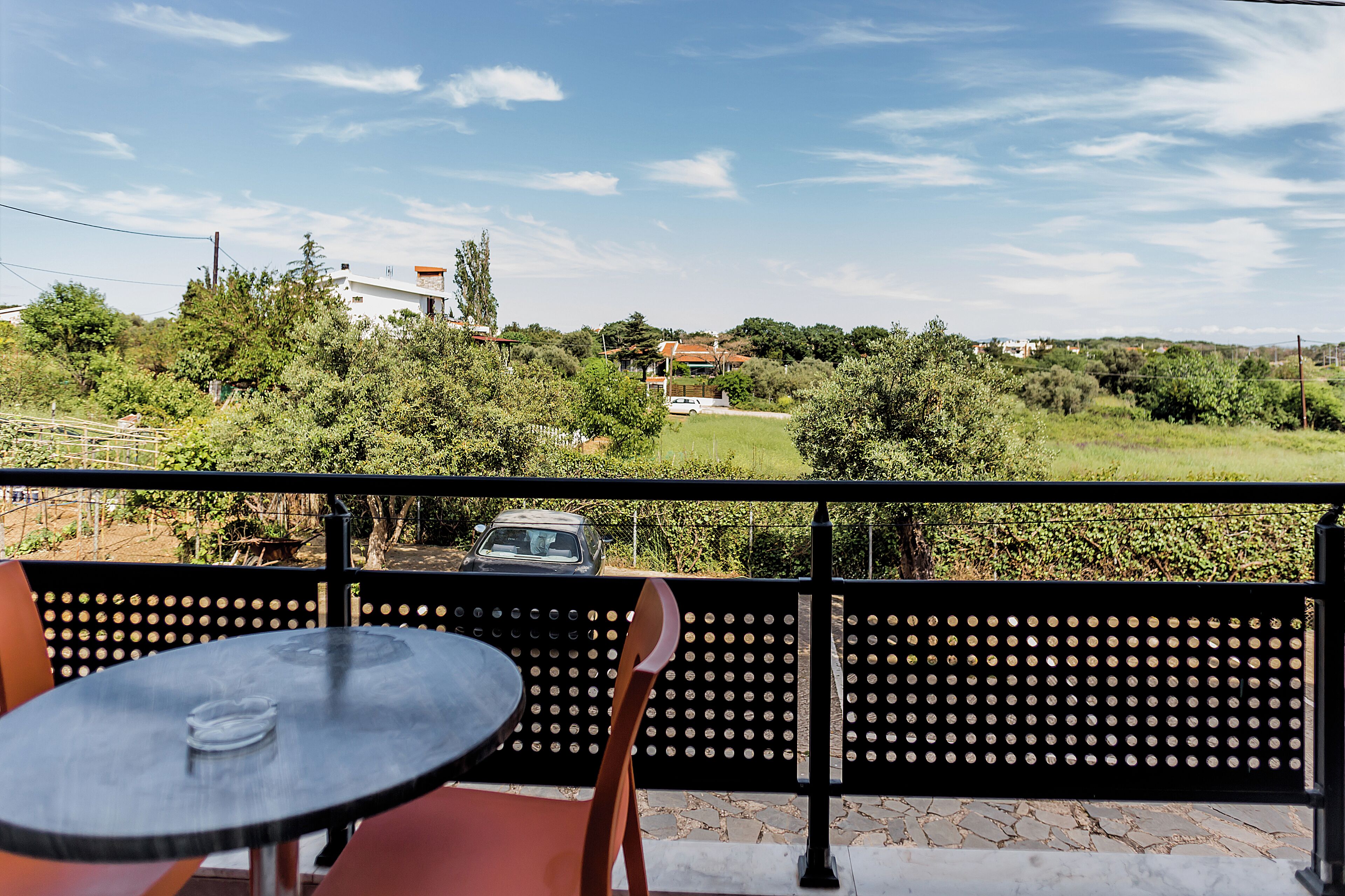 Ein Balkon mit Tisch und Stühlen, mit Blick auf eine grüne Landschaft mit Bäumen und einem Gebäude in der Ferne.