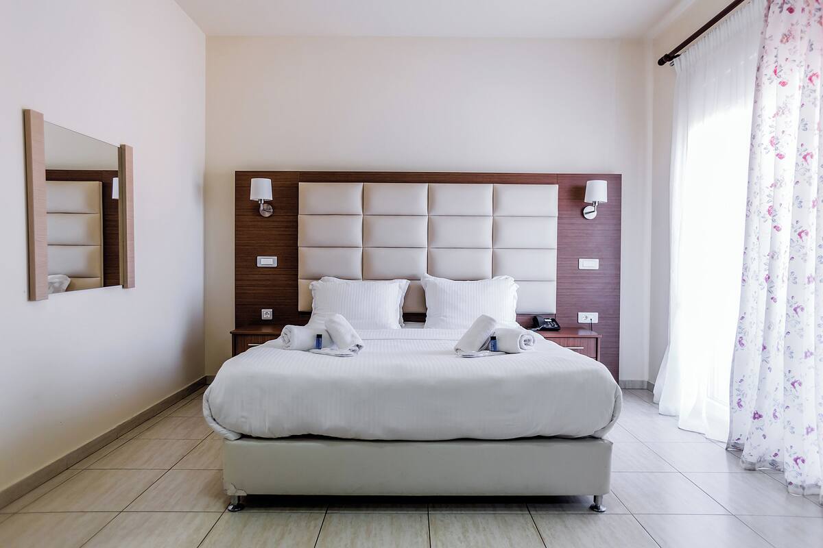 Un lit double avec une tête de lit en bois, deux tables de chevet avec des lampes et un grand miroir sur le mur de gauche.