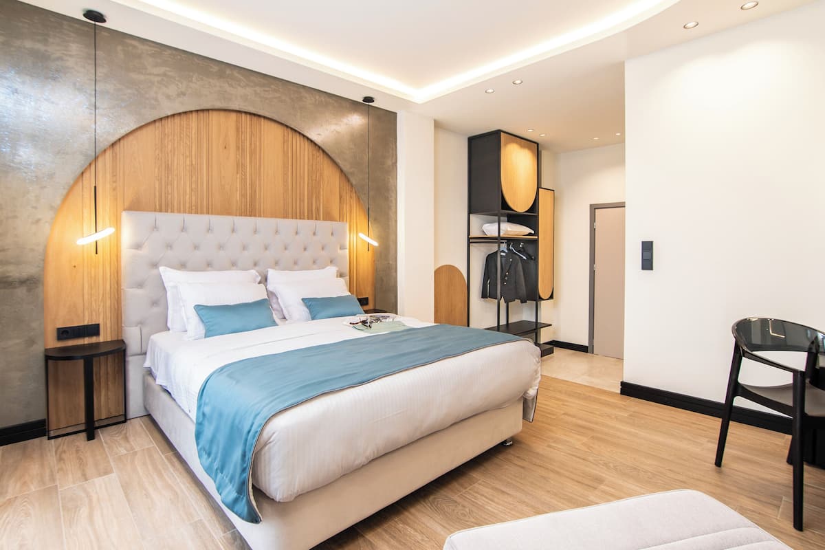 Une chambre moderne avec un grand lit, une tête de lit en bois aux lignes courbes, une petite table de chevet et une armoire avec un miroir.