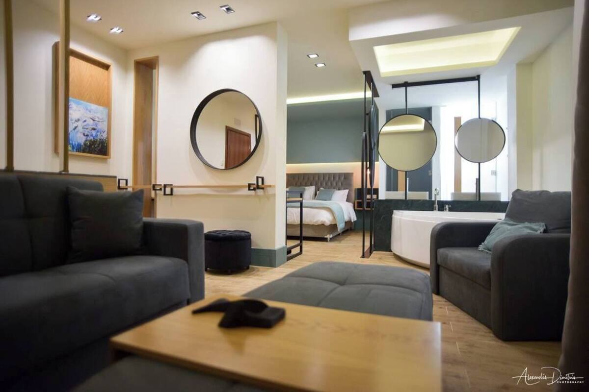 Une chambre d’hôtel moderne avec un canapé, une petite table, un lit avec une tête de lit et deux miroirs ronds.