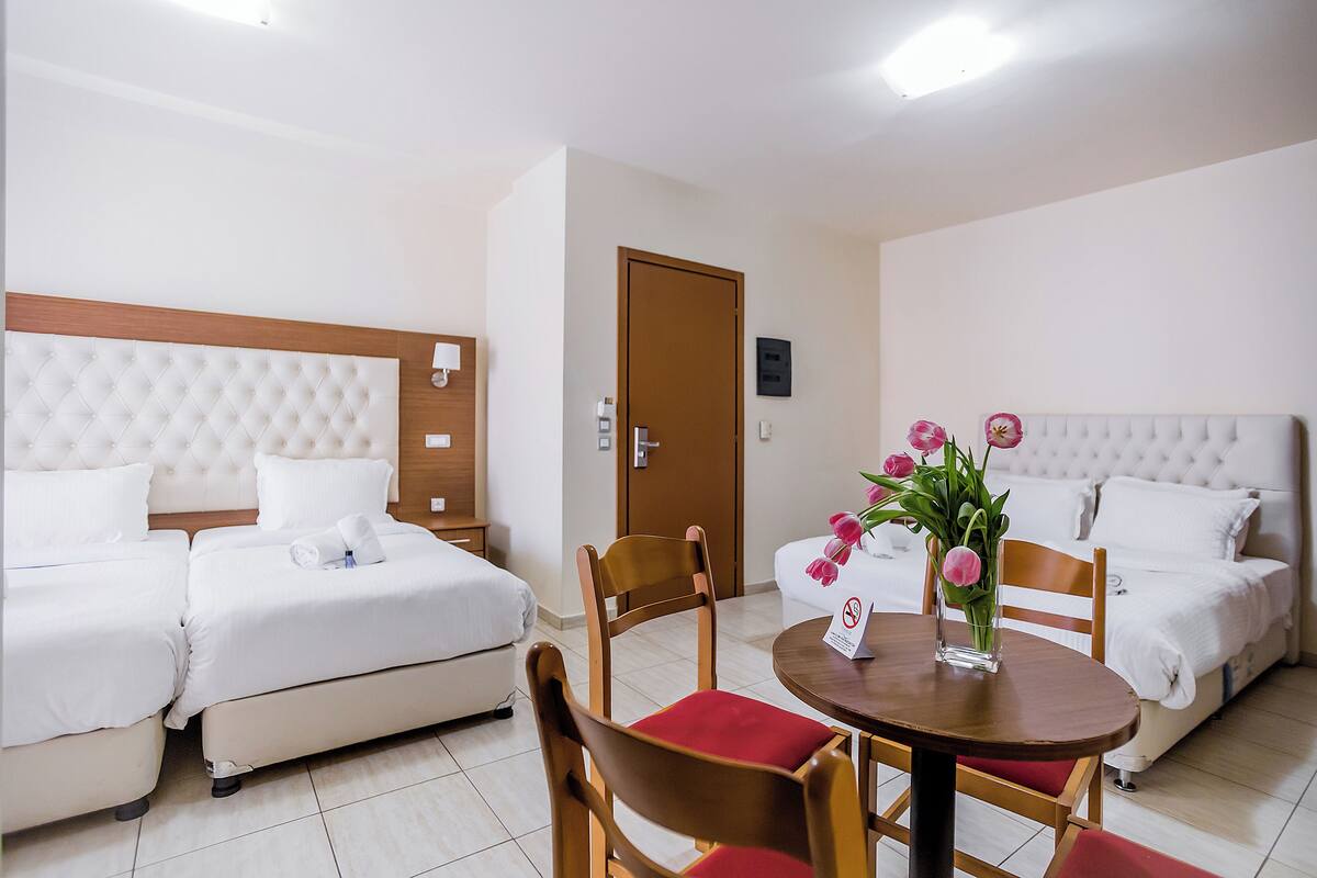 Une chambre d’hôtel avec deux lits, une chaise en bois, une petite table sur laquelle est posé un vase de fleurs, et une porte.