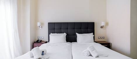 Une chambre d’hôtel avec un grand lit, deux tables de chevet, une tête de lit noire et des lampes blanches.