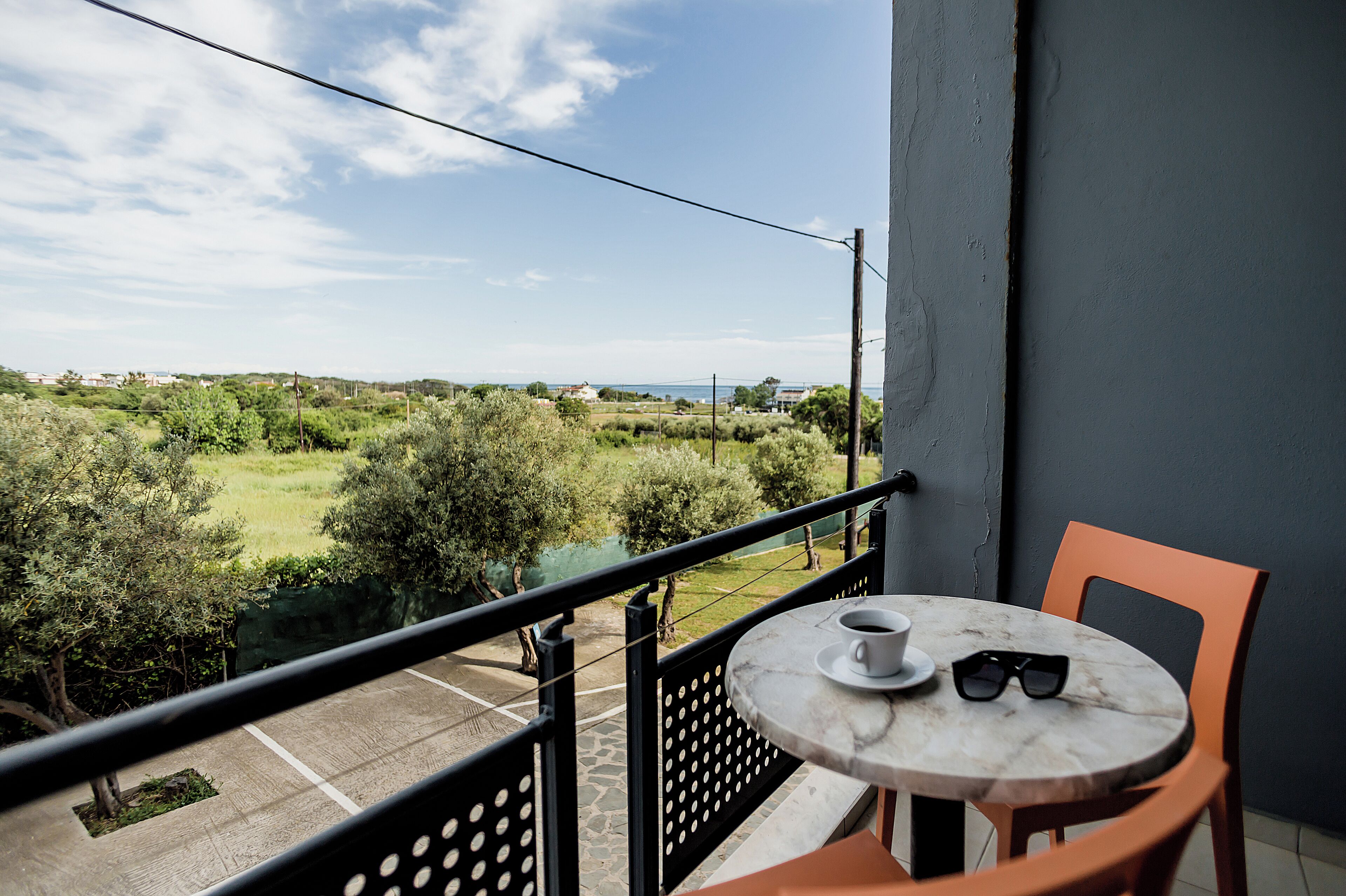 A balcony with a table and chairs, overlooking a green landscape and a body of water.