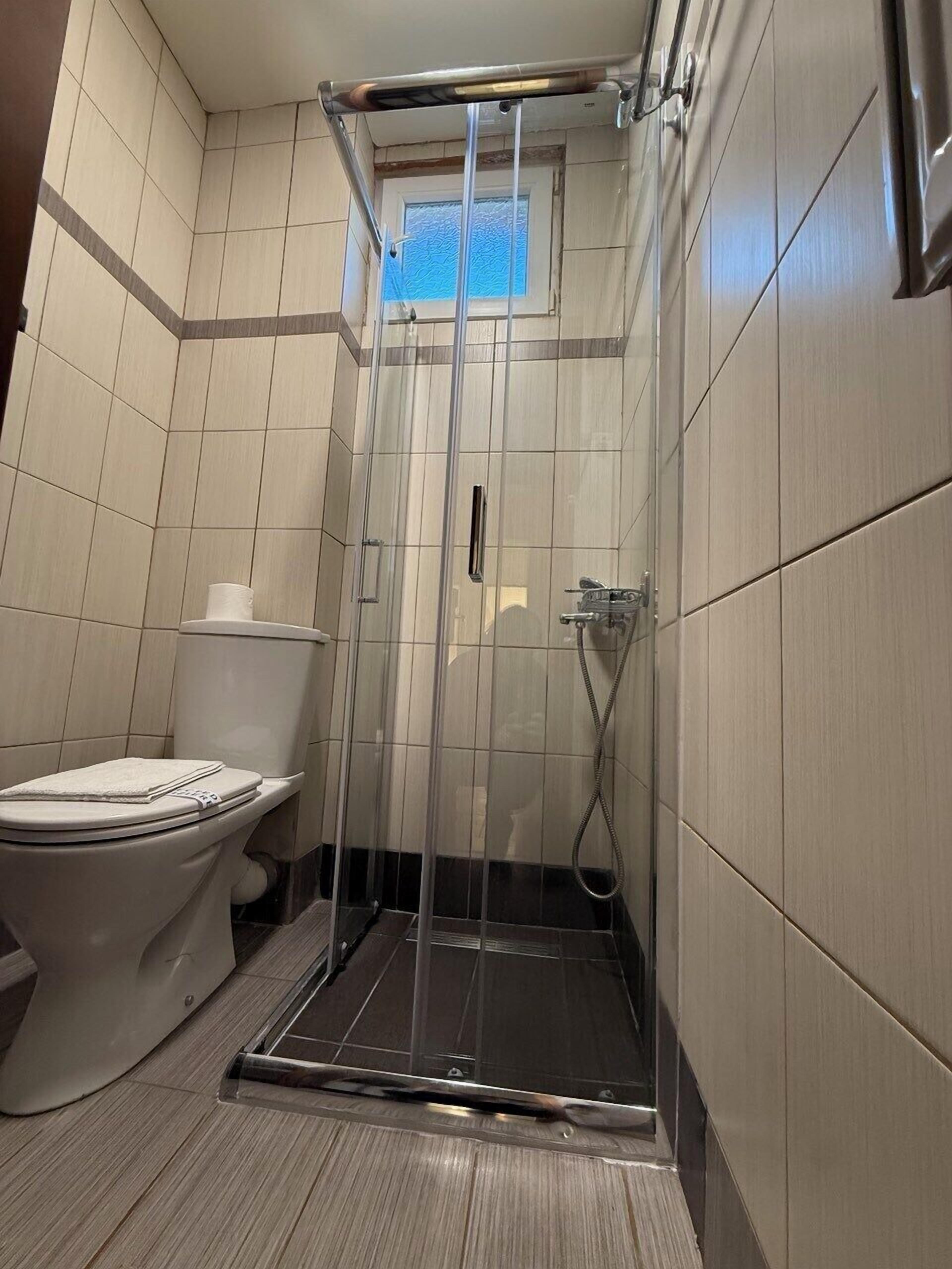 Et badeværelse med et glasafskærmet brusebad, toilet og et vindue.