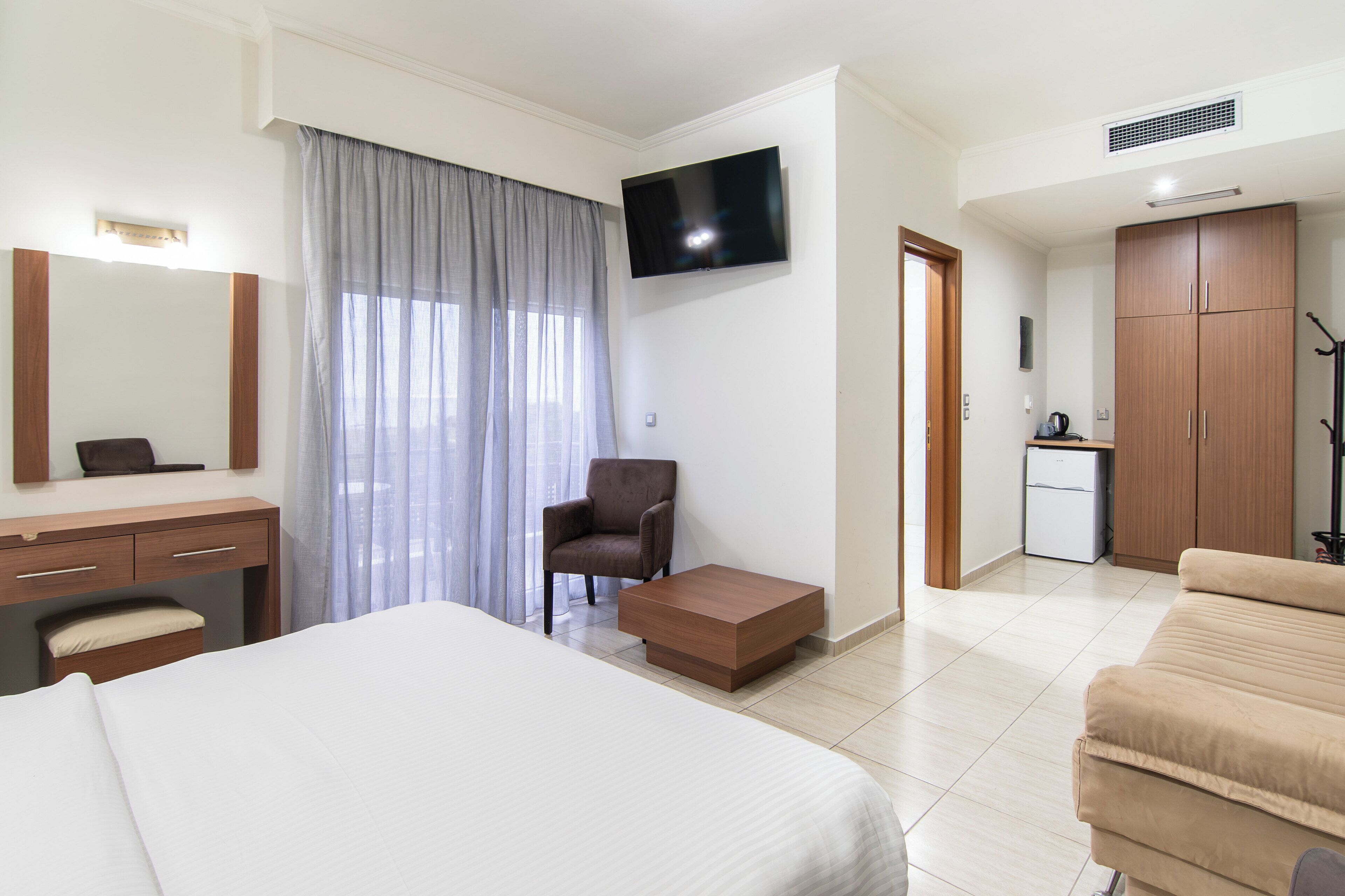 Habitació d'hotel amb llit, escriptori, cadira, televisió, petita cuina i armari.