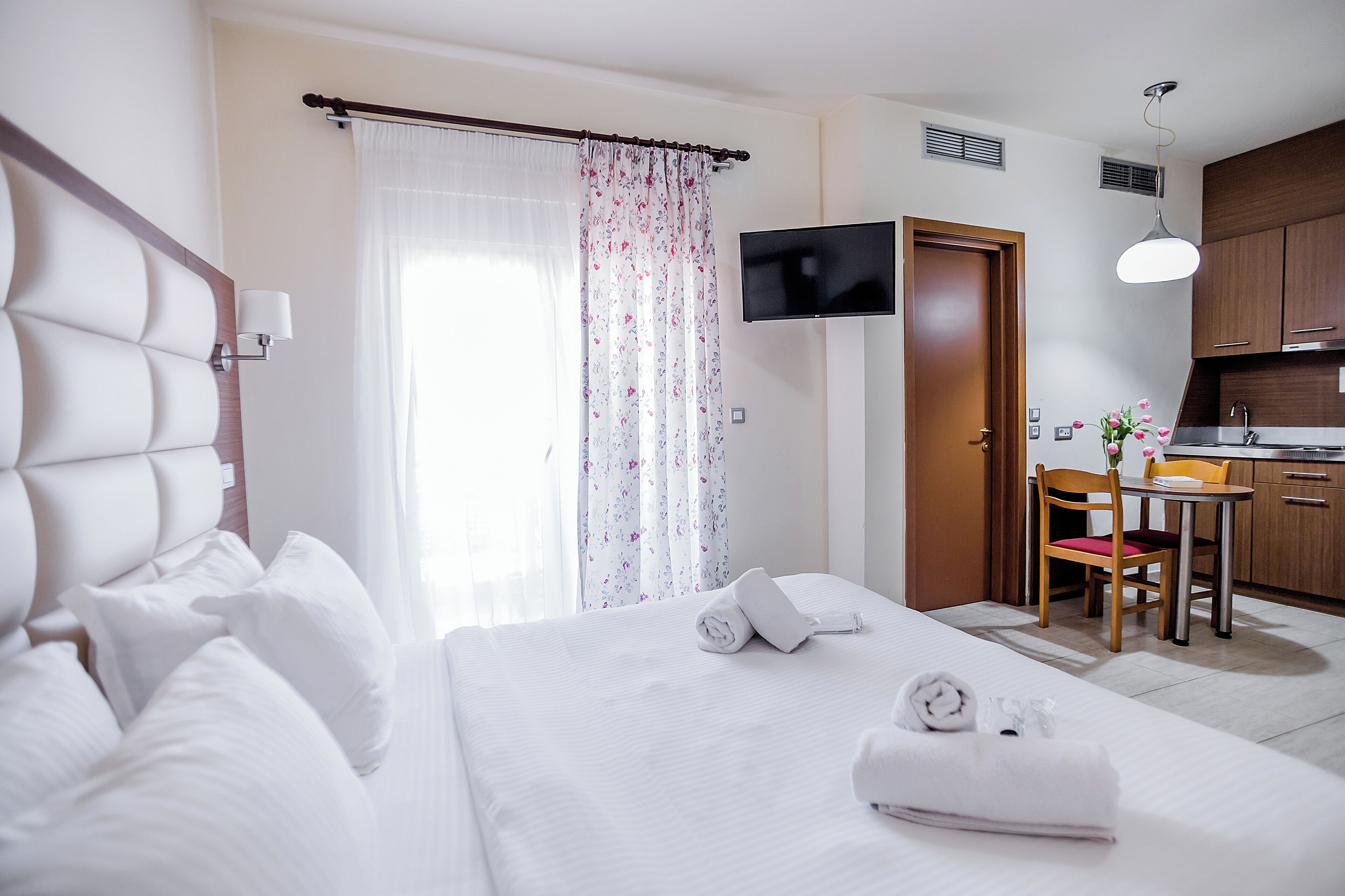 A hotel room with a bed, a TV, a desk with a chair, and a kitchenette.