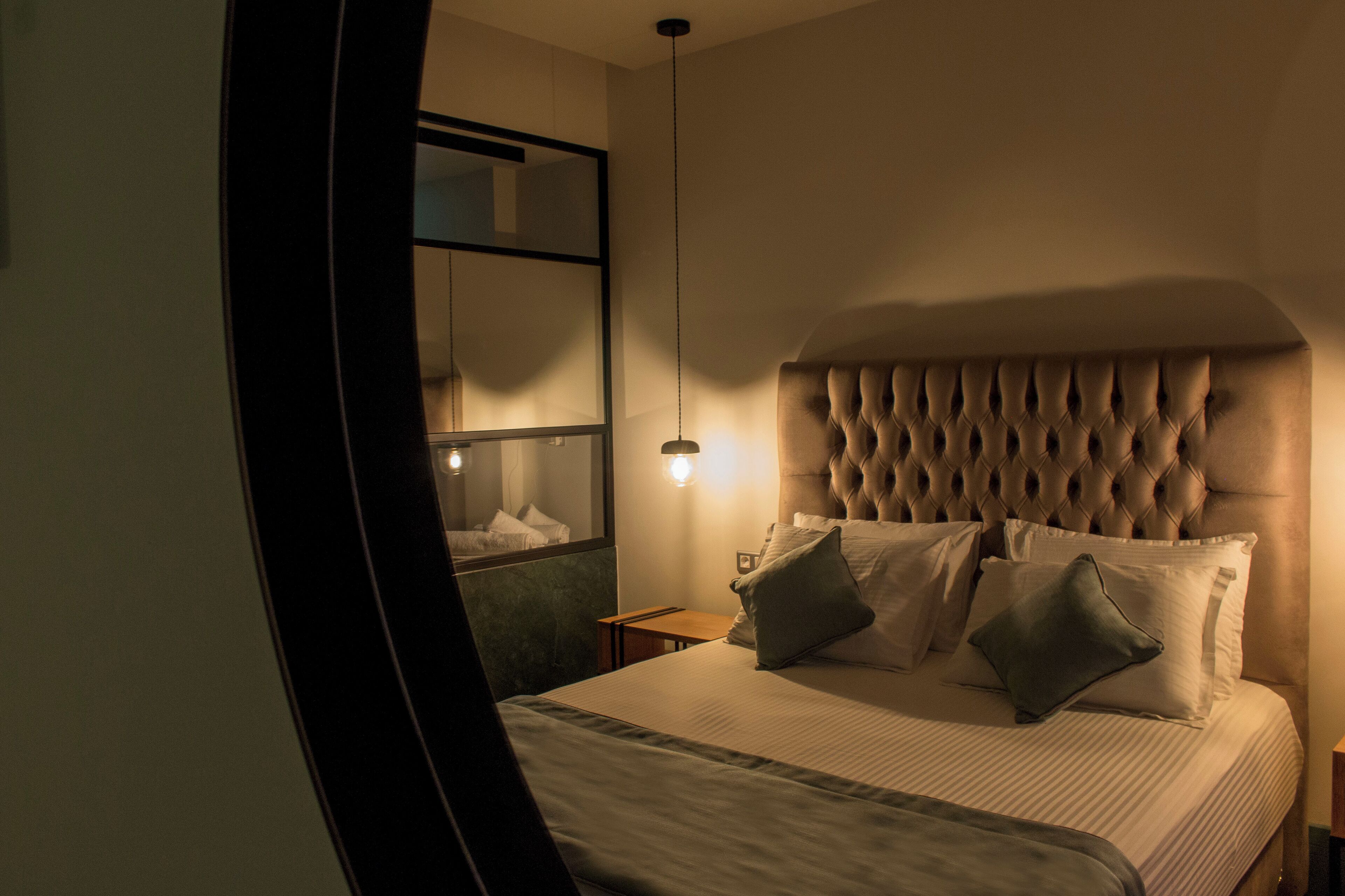 A neatly made bed with a tufted headboard, a bedside table, and a wall-mounted mirror.
