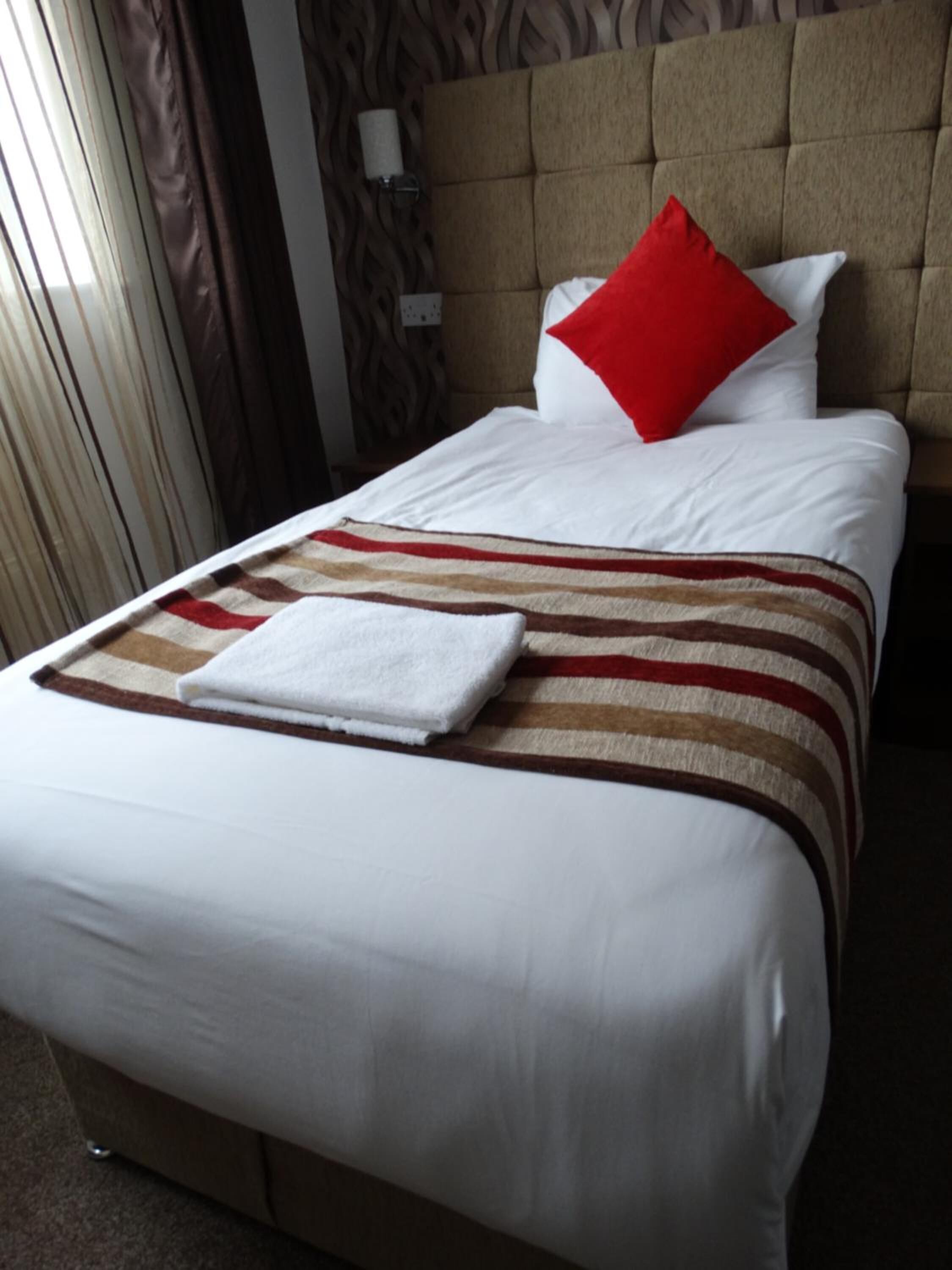A neatly made bed with white linens, a striped blanket, and a red pillow.