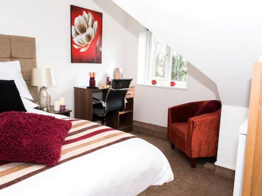 Een slaapkamer met een bed, een bureau, een stoel en een raam.