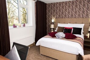 A hotel room with a bed, curtains, a window, a lamp, and a patterned wall. - Trivelles Mayfair (Stockport)