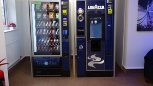 Ein Automatenbereich mit zwei Lavazza-Automaten, einer für Getränke und einer für Snacks, in einer gewerblichen Umgebung.