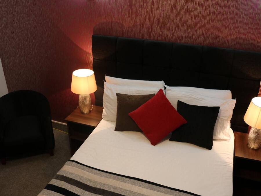 A neatly made bed with white and black bedding, two bedside lamps, and a red pillow.