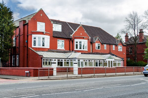 A red brick building with a large bay window and a covered front porch. - Trivelles Mayfair (Stockport)