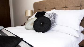 A neatly made bed with white bedding and multiple pillows, including a black one with a decorative center.