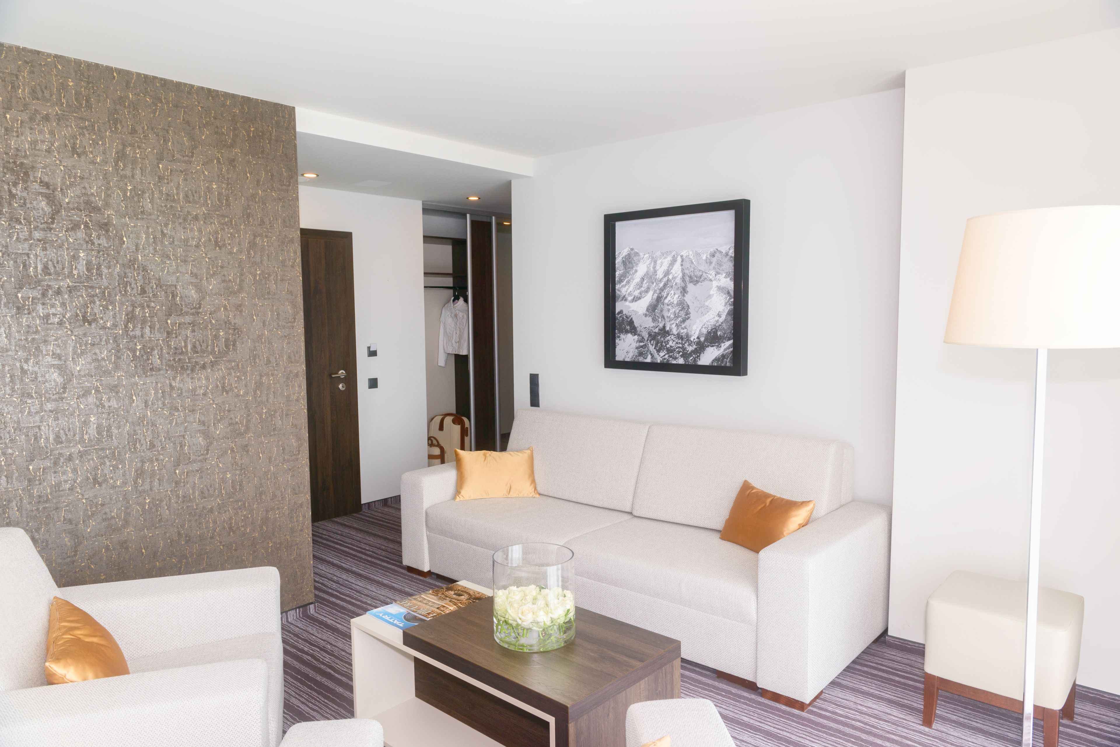A modern hotel room with a white sofa, a coffee table, and a large abstract wall art piece.