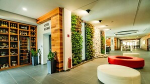 A hotel lobby with a wooden reception desk, a wall-mounted plant display, and a seating area with white and red ottomans. - Hotel Horizont Resort (Stara Lesna)