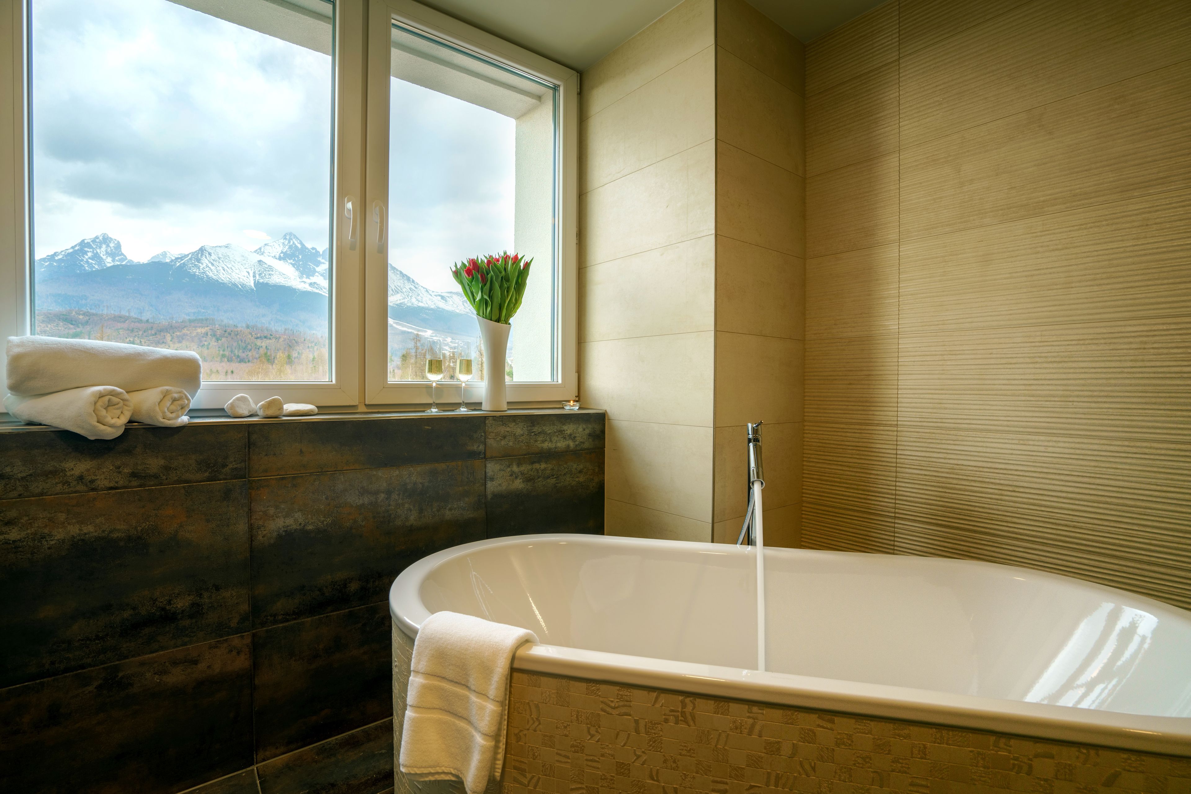 Un baño con bañera, ventana con vistas a montañas y un jarrón con flores.