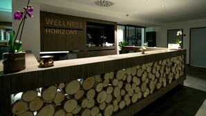 A reception desk with a wooden log display and a sign reading "WELLNESS HORIZONT". - Hotel Horizont Resort (Stara Lesna)