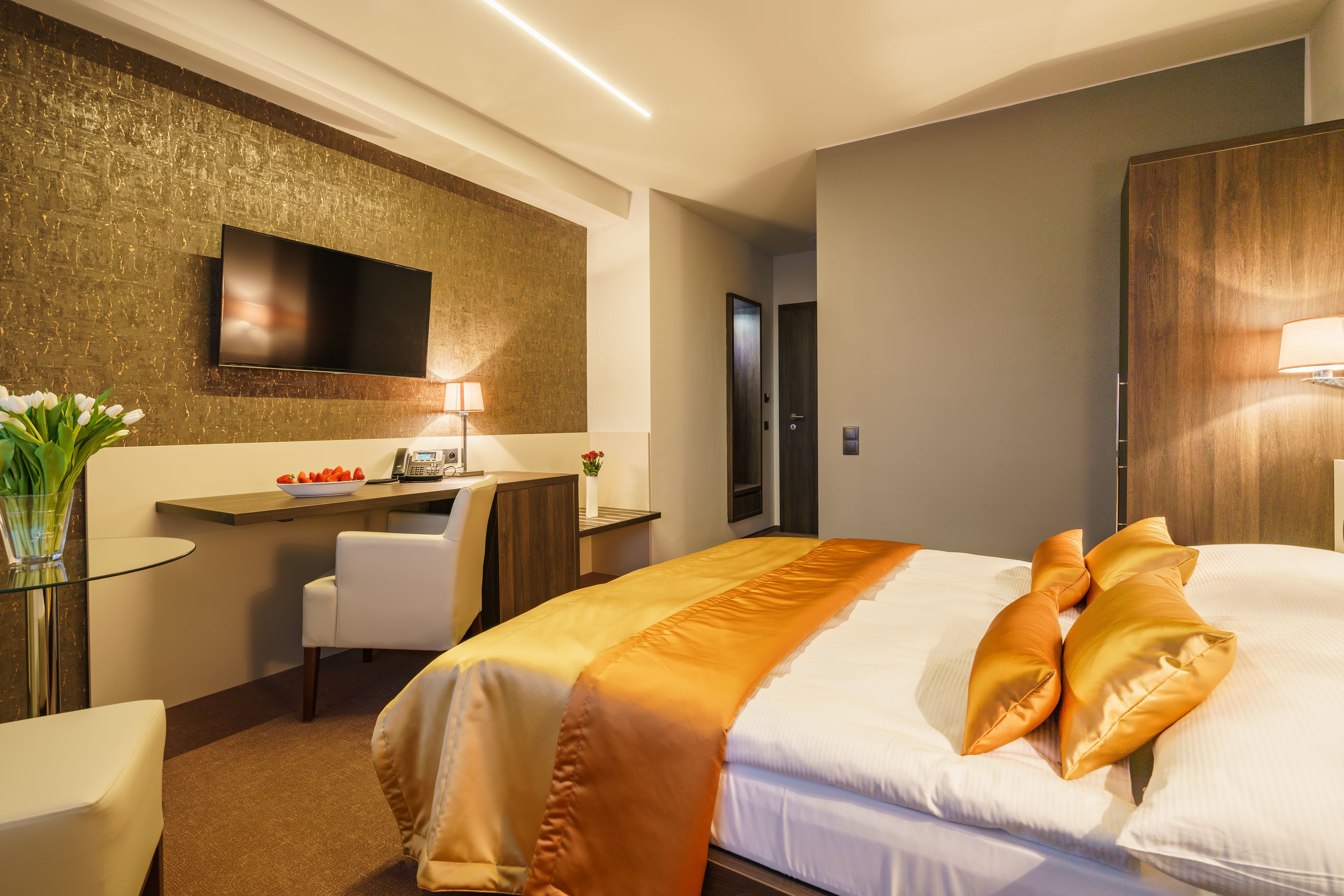 Habitación de hotel con una cama grande, un escritorio con silla, un televisor de pantalla plana en la pared y un armario de madera.