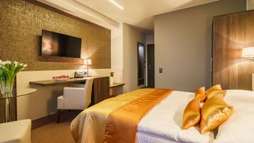 A hotel room with a large bed, a desk with a chair, a flat-screen TV mounted on the wall, and a wooden wardrobe.
