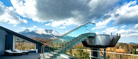 A modern staircase with glass railings leading to a balcony overlooking a mountainous landscape.