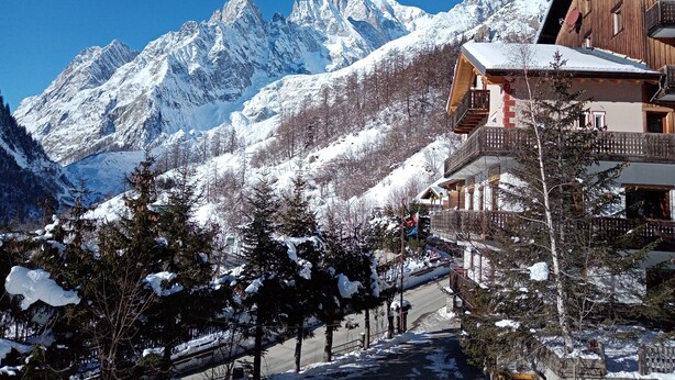 A mountain lodge with a snow-covered roof, wooden balconies, and a view of snow-capped peaks. - Hotel Astoria (Courmayeur)