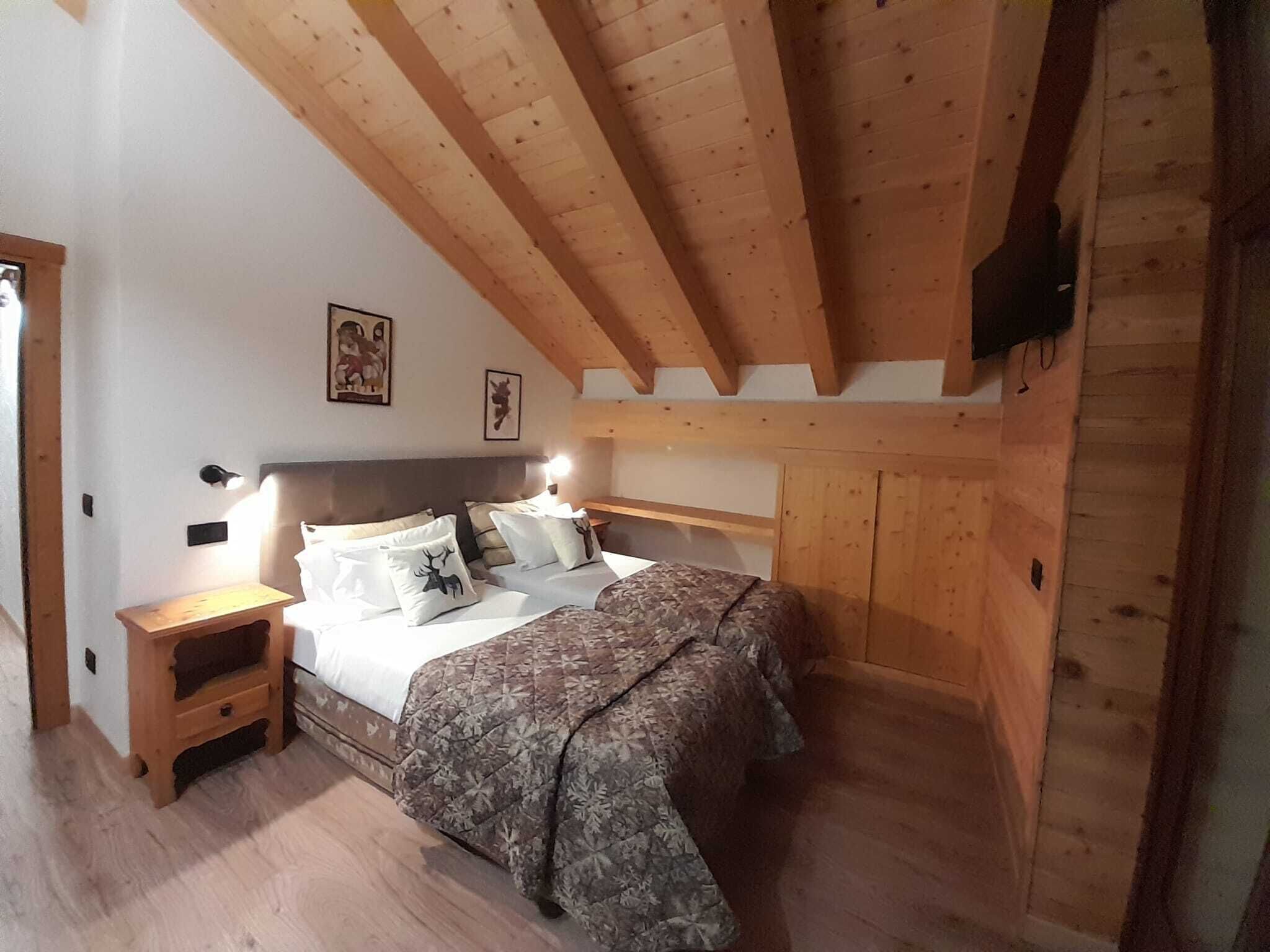 A bedroom with a wooden ceiling, a bed with patterned bedding, a nightstand, and a wall-mounted TV.