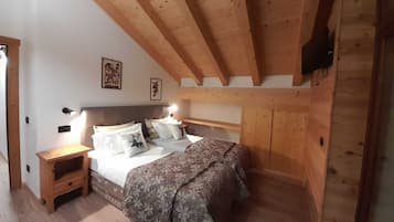 A bedroom with a wooden ceiling, a bed with patterned bedding, a nightstand, and a wall-mounted TV.
