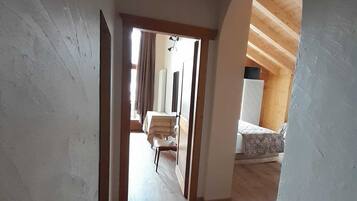 Un pasillo estrecho con suelo de madera que conduce a un dormitorio con cama y ventana.