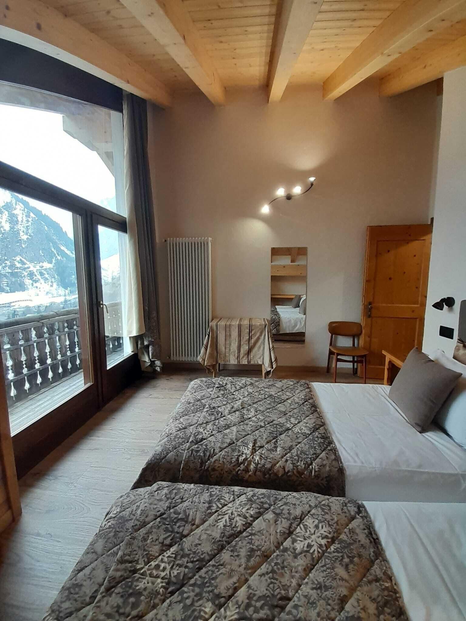 Et værelse med to senge, trælofter, et vindue med udsigt til bjerge, en radiator og et lille bord med en stol.
