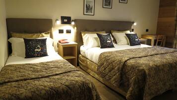 Two double beds with patterned bedding, bedside tables with lamps, and framed pictures on the wall.