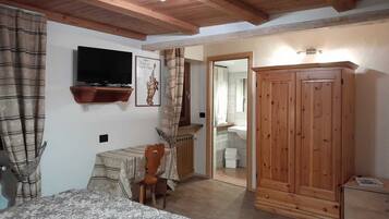 A bedroom with a bed, a wooden wardrobe, a television mounted on the wall, and a bathroom visible through an open door.