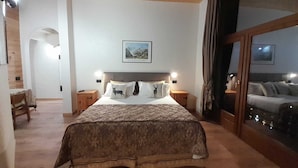 A bedroom with a large bed, wooden beams, a nightstand, a bedside table, a framed picture on the wall, and a view through a glass door. - Hotel Astoria (Courmayeur)