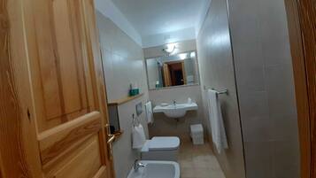 Un baño pequeño con puerta de madera, un lavabo, un inodoro y zona de ducha.