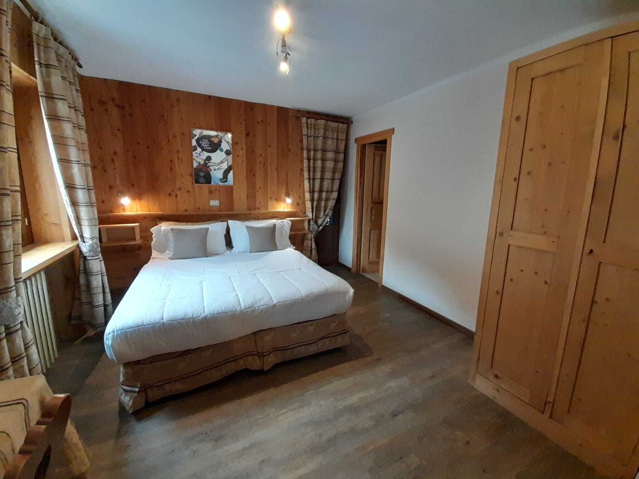 A bedroom with a large bed, wooden walls, a wooden wardrobe, and a small bedside table.